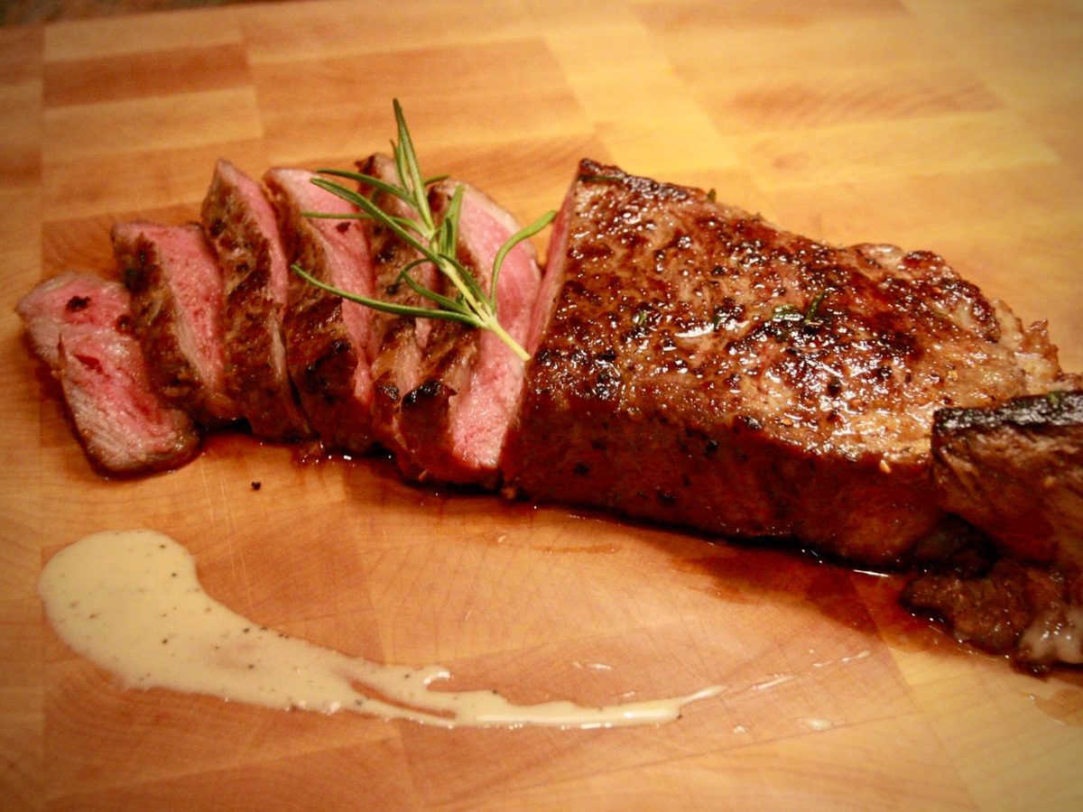 A sliced steak with rosemary on a cutting board